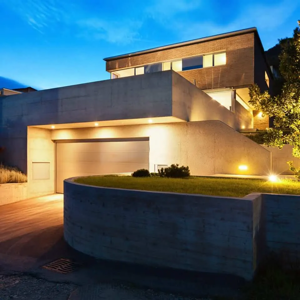 Brüt beton duvarları, tuğla cephe detayları, kapalı garajı ve peyzaj aydınlatmaları bulunan eğimli arazide modern lüks villa